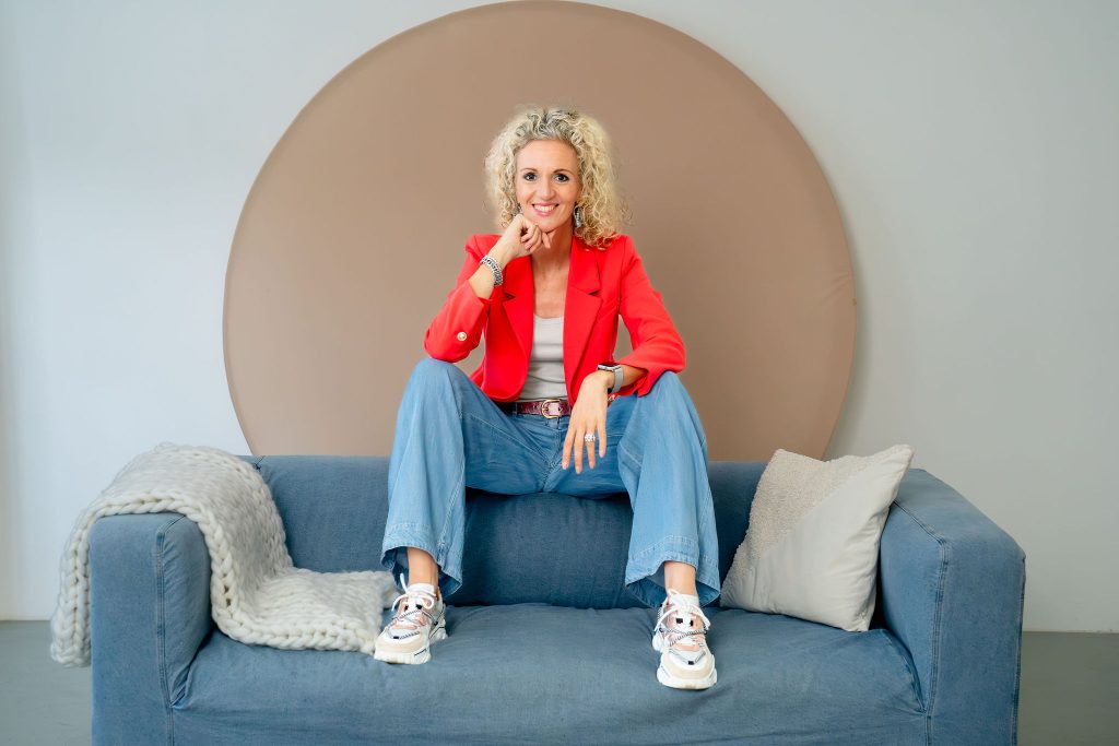Kleurrijke fotoshoot waar styling en energie samenkomen. De jurk met vrolijke patronen en de felroze achtergrond versterken de creatieve vibe.